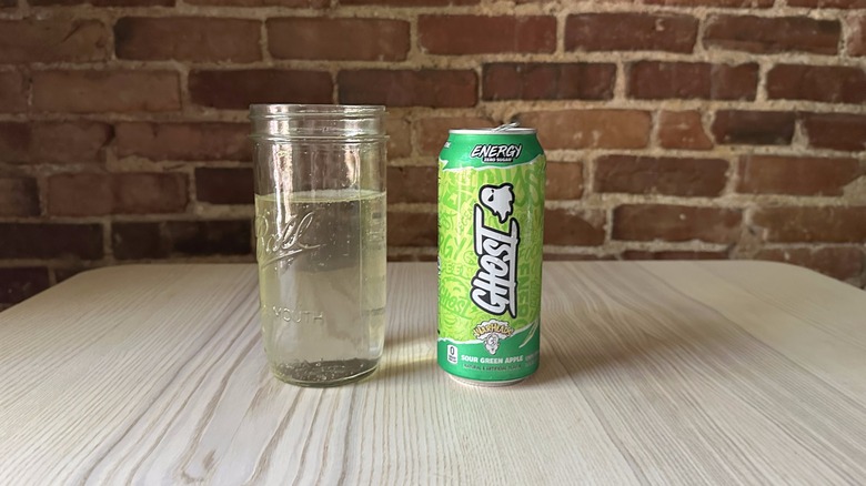 A can of Ghost Energy's Warheads Sour Green Apple flavor next to a glass of the drink.