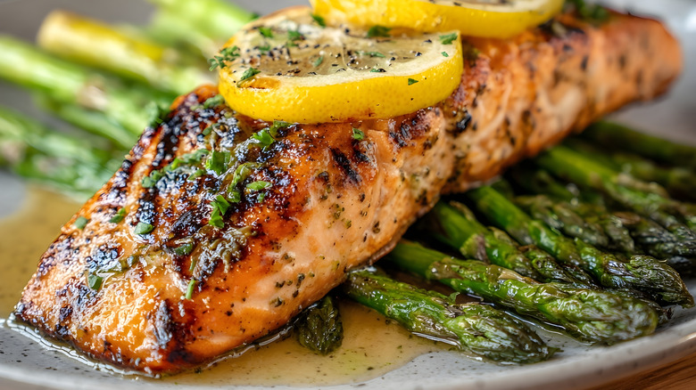 A filet of salmon with herbs, spices, and lemon slices on top of asparagus