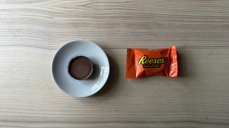 A Reese's peanut butter cup on a plate next to the wrapper