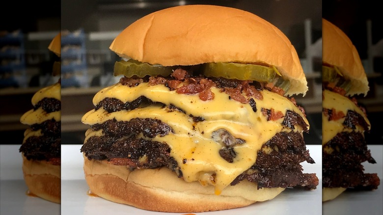 Burger with three patties, cheese, bacon, and pickles