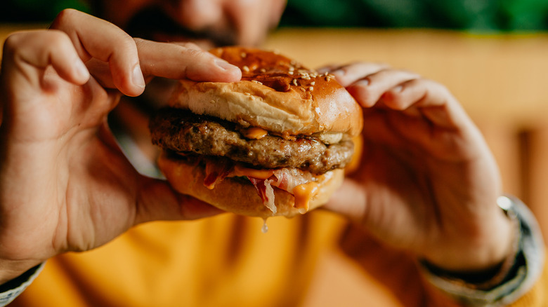 Close-up of two hands holding a burger with blurred person in background