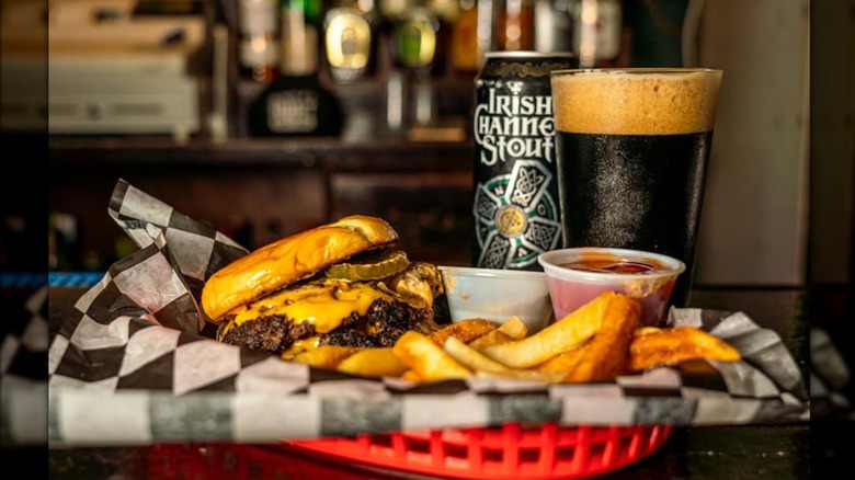 Burger with cheese and pickles in a red tray with fries, ketchup, and a beer