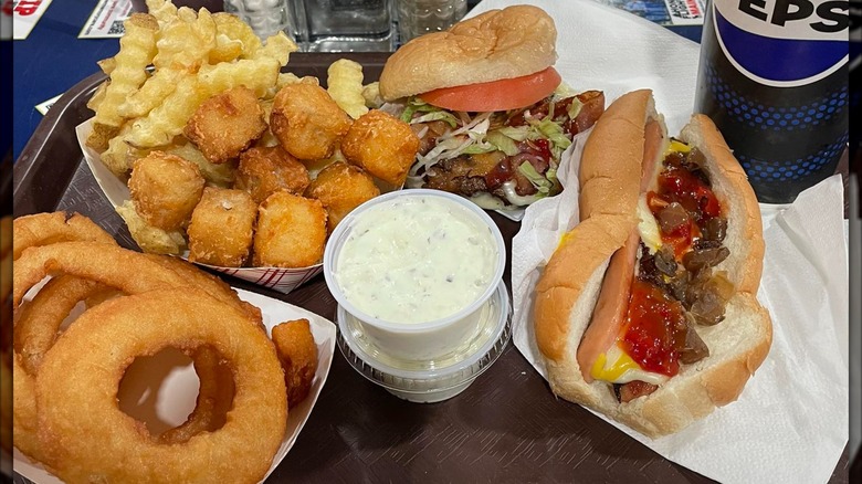 Table with a burger, hot dog, onion rings, fries, tots, and sauce