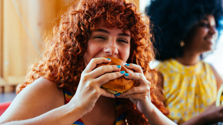 Person eating a burger with another person blurred background