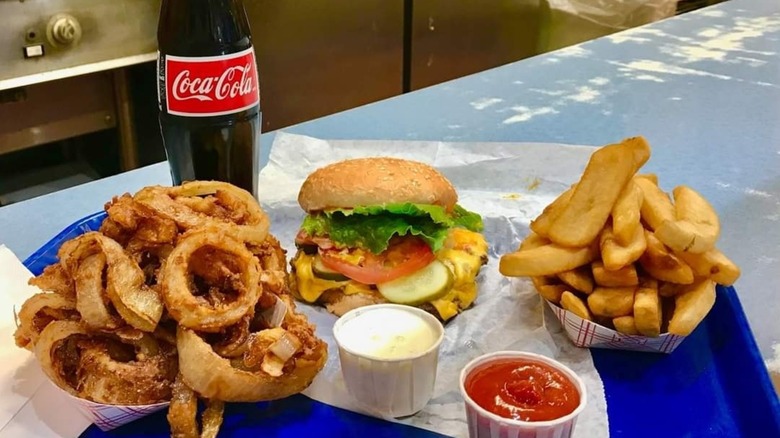 Onion rings, fries, burger, ketchup, mayo, and bottle of Coke on blue tray