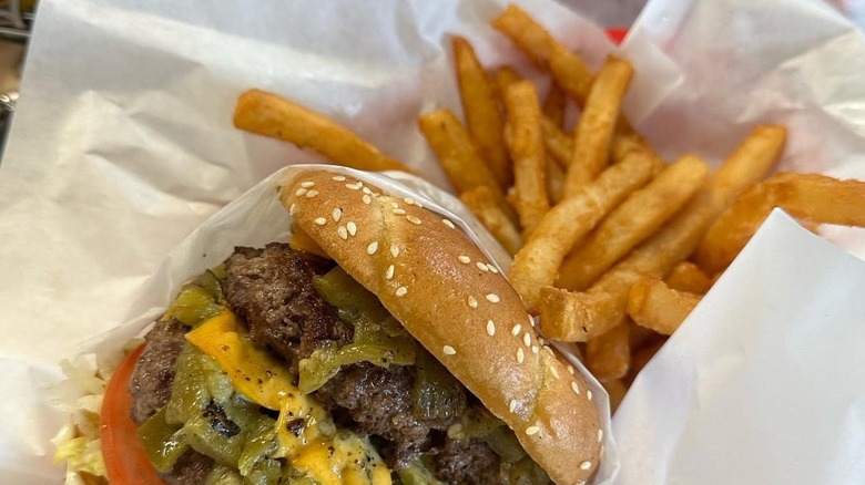 Burger with green chile, cheese, tomato, and fries in paper
