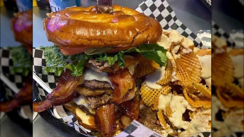Huge burger with bacon and lettuce on tray with cheesey chips