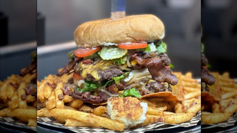 Massive burger with tomatoes, pickles, cheese, bacon, and lettuce on a pile of fries