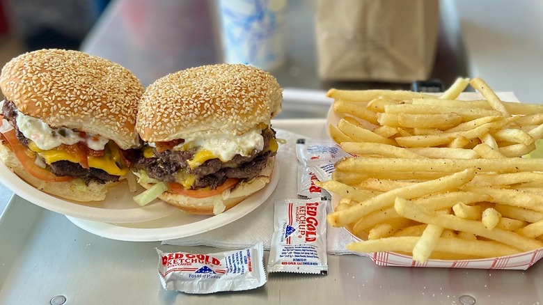 Two burgers with tomato and cheese on plate and tray with fries