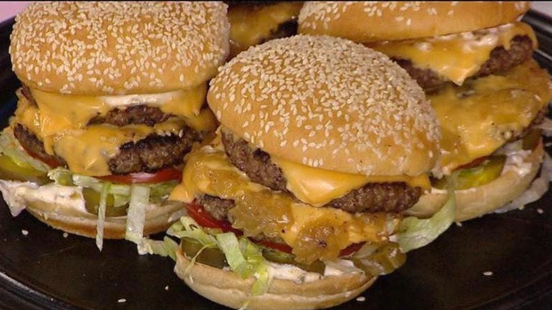 Three double cheeseburgers with sesame seed buns on black plate