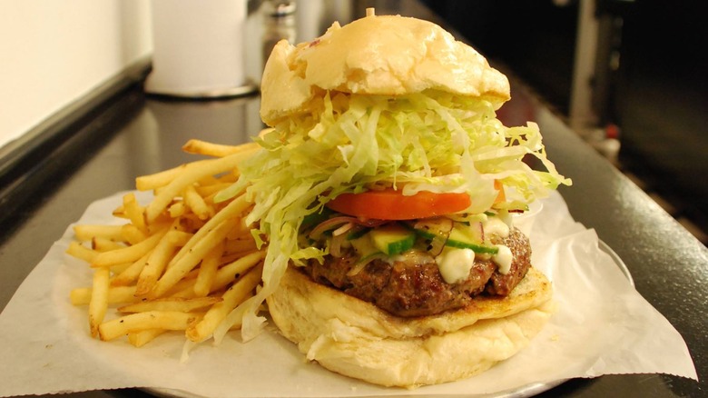 Burger with lettuce, tomato, and pickles on tray with fries