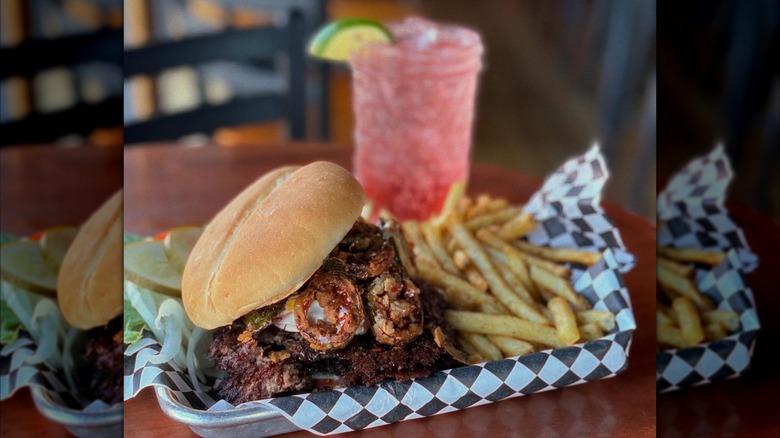 Popper Burger with jalapeños and fries on a tray and a cocktail in the background
