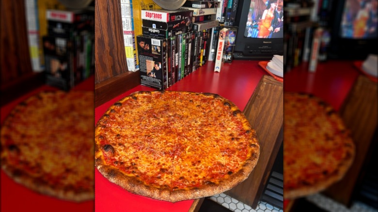 Cheese pizza on a red counter alongside a television and VHS tapes