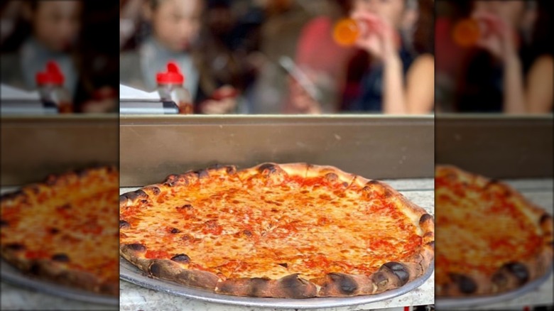 New York-style pizza on a tray with customers in the blurred background