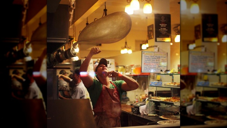 Person throwing dough in the air to make pizza crust in a dimly lit pizzeria kitchen