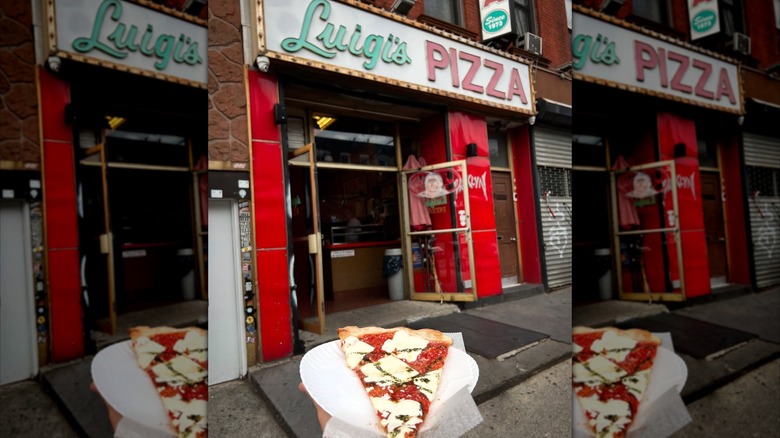 Hand holding a slice of pizza in front of the Luigi's storefront