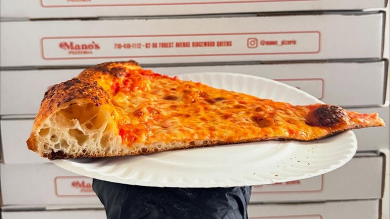Single slice of pizza on a paper plate in front of a stack of pizza boxes