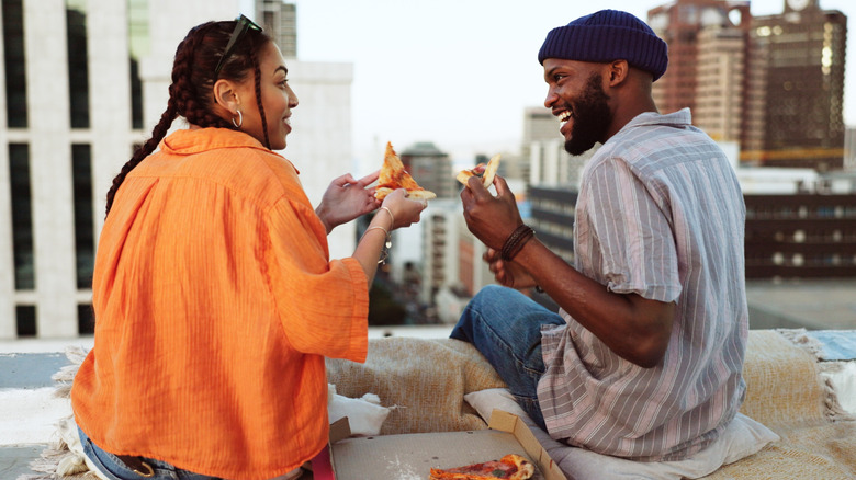 Two people eating New York-style slices on a NYC rooftop