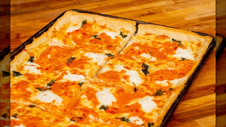 Square pizza in a tray sitting on a wood-grain counter