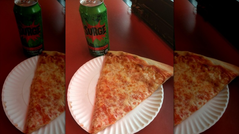 Slice of pizza on a paper plate with a can of soda