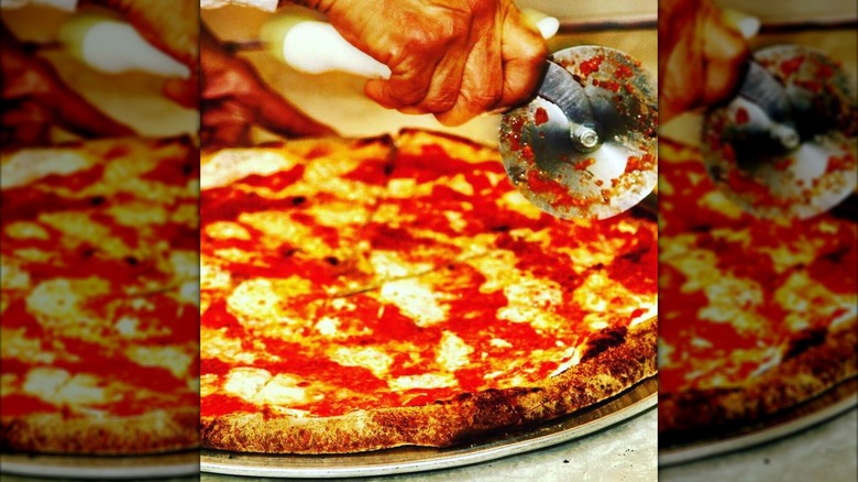 New York-style pizza being cut by hand with a pizza wheel