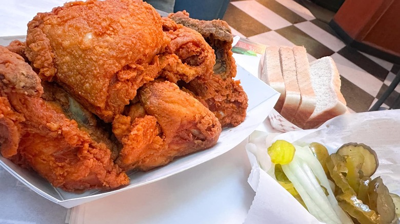 Container of fried chicken with side of pickles and white bread