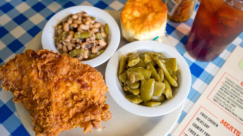 Piece of fried chicken with sides and biscuit on blue and white tablecloth