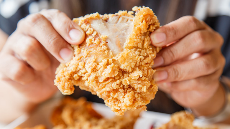 Hands breaking apart a piece of fried chicken