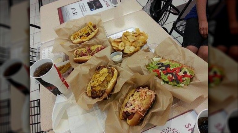 Harley's Peppy's Pizza Dog and Chili Cheese Tots in a red plastic basket, with other hot dogs in the background