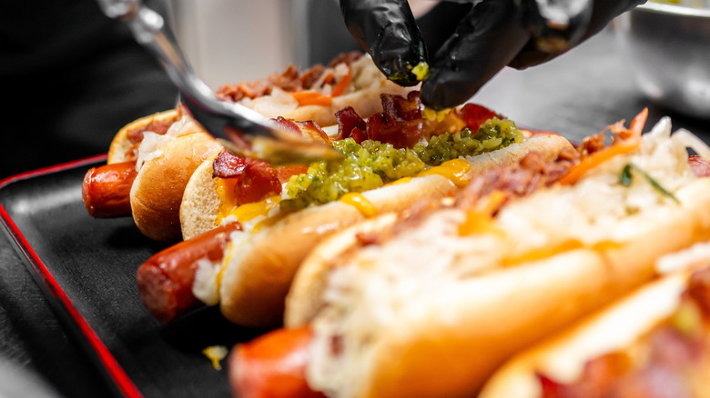 Chef adding interesting toppings to a row of hot dogs