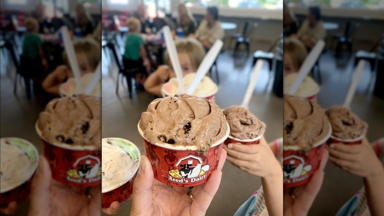 Hands holding four bowls of ice cream with varying flavors in shop
