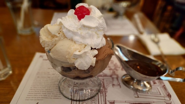 Brownie sundae featuring vanilla and chocolate ice cream, plus whipped cream, chocolate sauce, and cherry