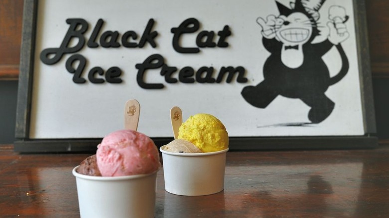 Four different flavors of ice cream distributed between two bowls in front of Black Cat Ice Cream logo