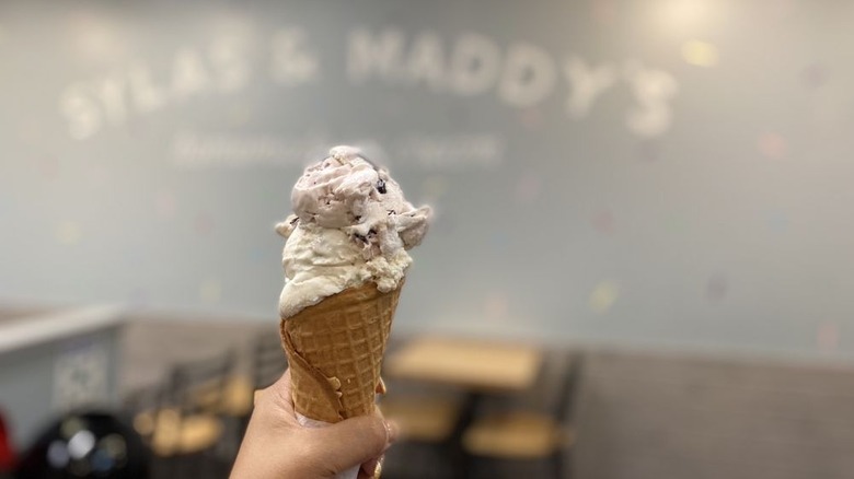 Hand holding waffle cone with two flavors of ice cream in shop