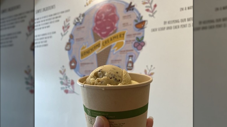 Hand holding cup of ice cream in front of Honeycomb Creamery mural
