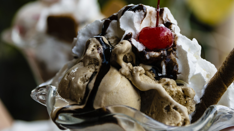 Ice cream sundae in glass bowl topped with chocolate syrup, whipped cream, and cherry