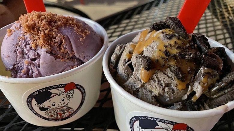 Two cups of ice cream with toppings on picnic table