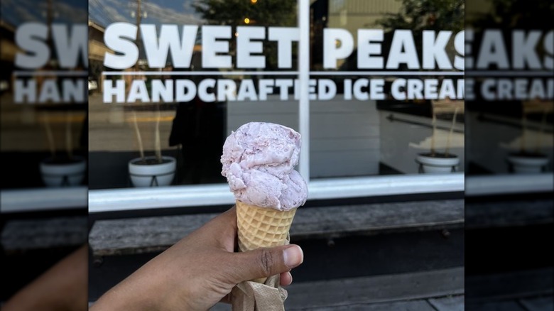 Hand holding huckleberry ice cream in cone in front of Sweet Peaks storefront