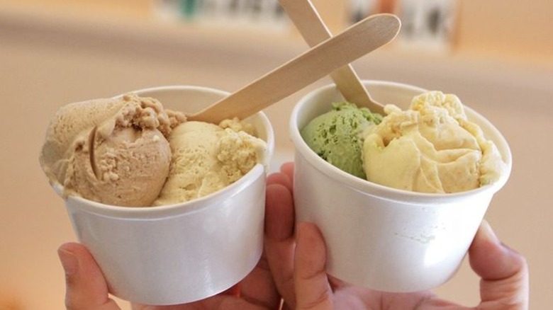 Two hands holding two cups of ice cream with various flavors