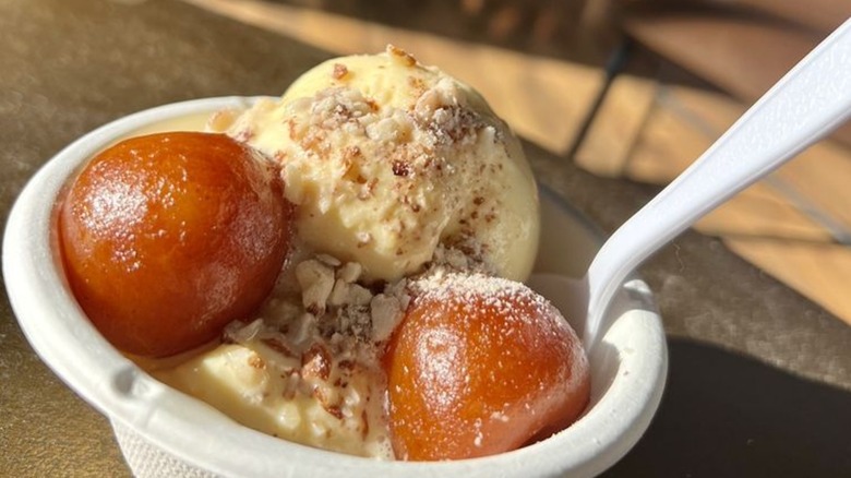 Two gulab jamun in bowl with mango ice cream and spoon