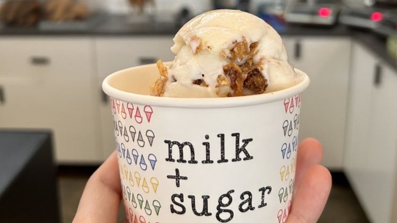Hand holding ice cream cup in shop with waffle cone makers in background