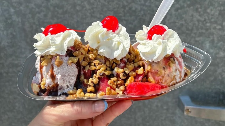 Hand holding banana split topped with nuts, chocolate syrup, whipped cream, and cherries