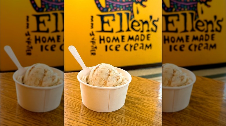 Cup of banana pudding ice cream on table in front of Ellen's Homemade Ice Cream mural