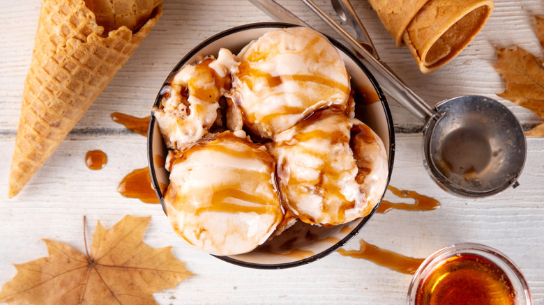 Aerial view of a bowl of maple ice cream surrounded by sugar cones, maple leaves, and scooper