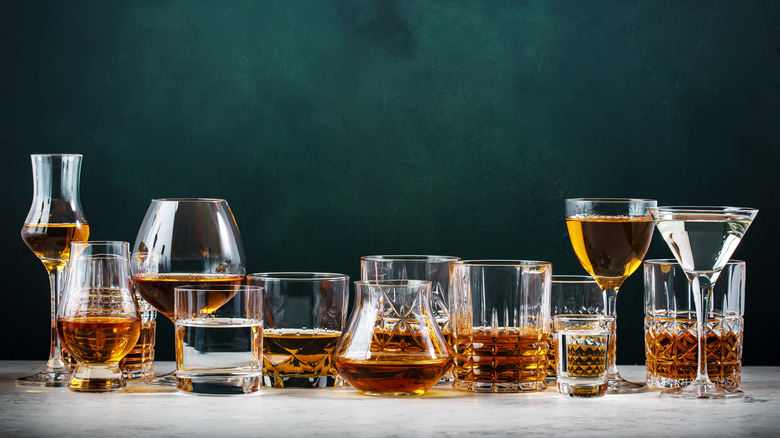 Various bar glasses holding different liqueurs and spirts clustered together against dark background.