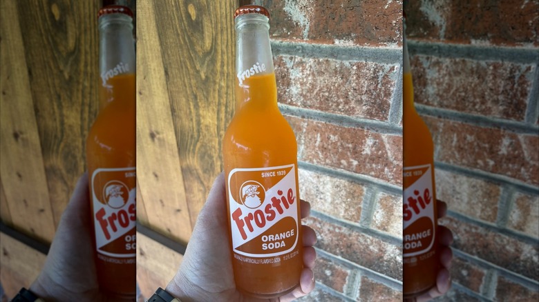 Hand holding a bottle of Frostie Orange Soda