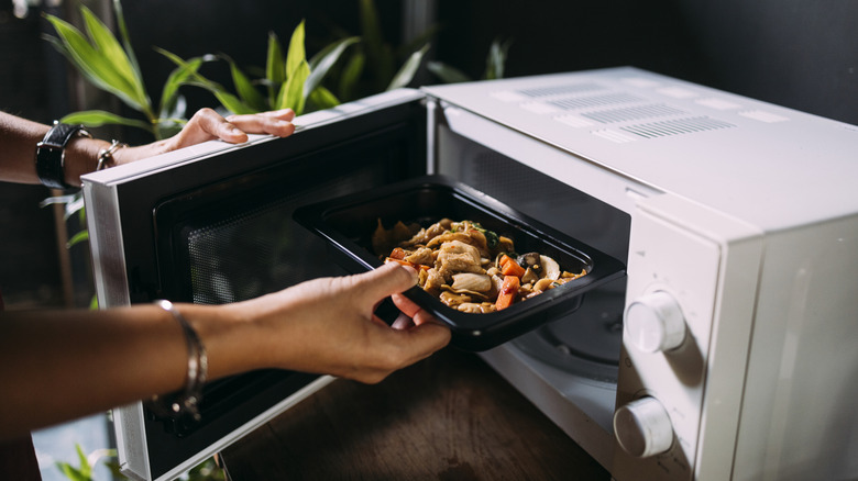 Woman puts container of leftovers in the microwave.