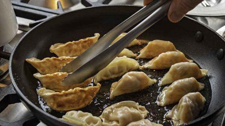 tongs being used to move dumplings shallow frying in a non-stick pan
