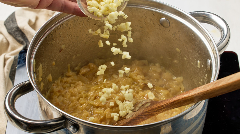 Overhead view of person adding garlic to pot of caramelized sliced onions