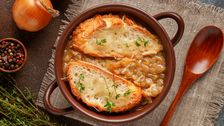 Dark red pot of onion soup with cheesy bread, alongside wooden spatula